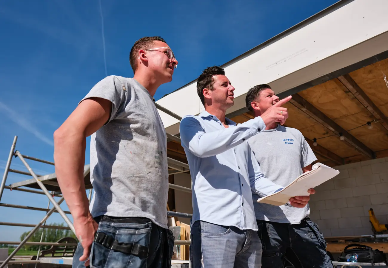 Drie bouwvakkers van Ter Beek Bouw overleggen op de bouwplaats tijdens de aanbouw van een woning.