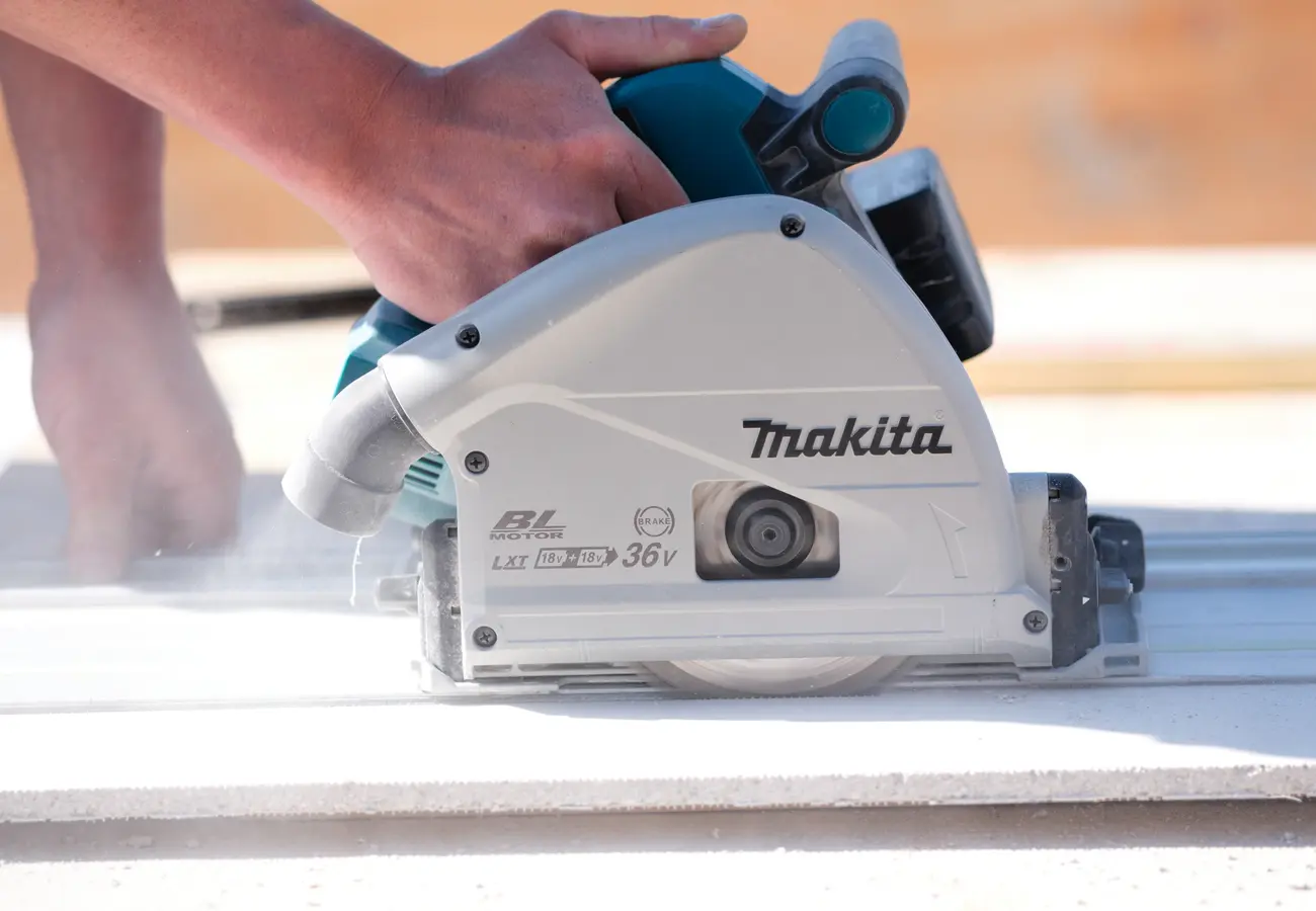 Vakman zaagt met een Makita accu-cirkelzaag een bouwplaat tijdens de bouw van een aanbouw.
