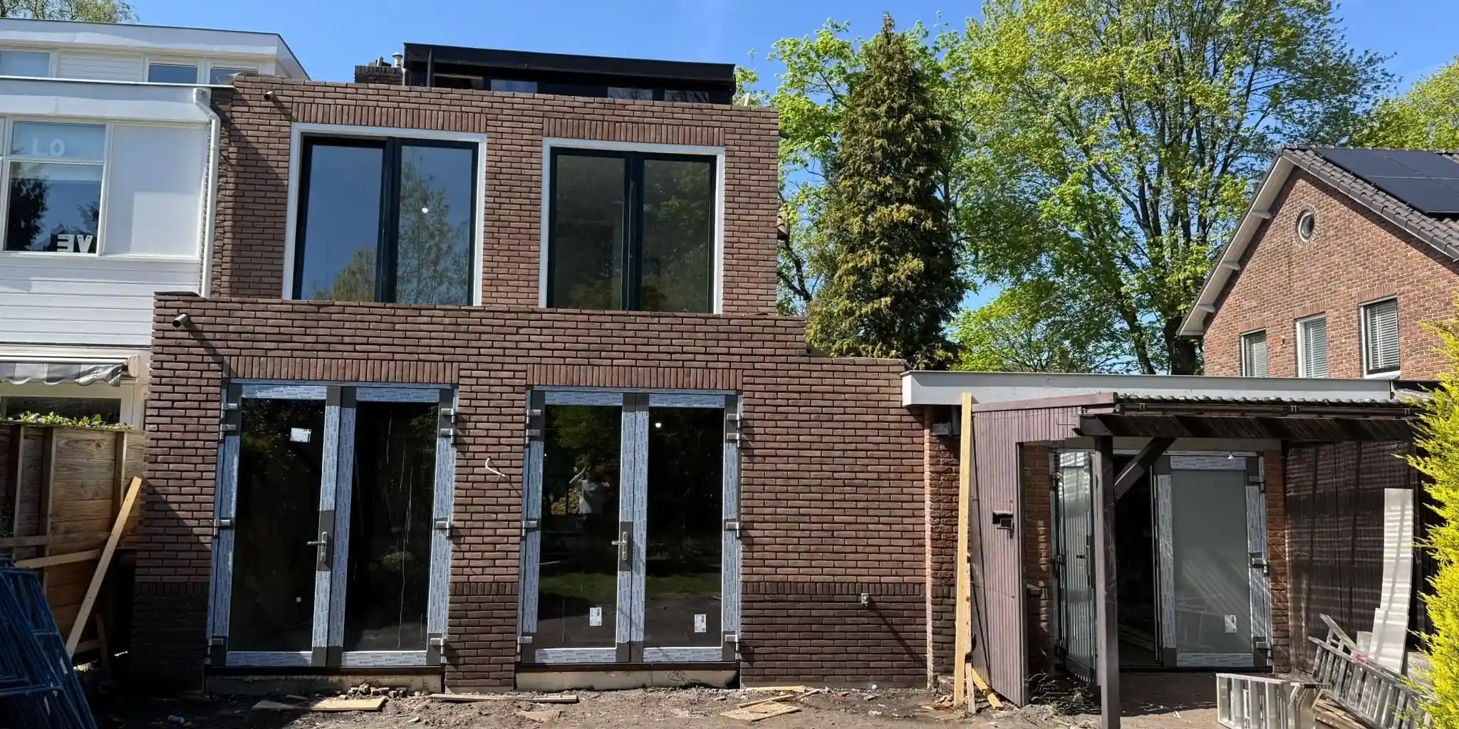 Nieuwe bakstenen gevel met grote raampartijen en openslaande deuren tijdens renovatie door AanbouwMaximaal