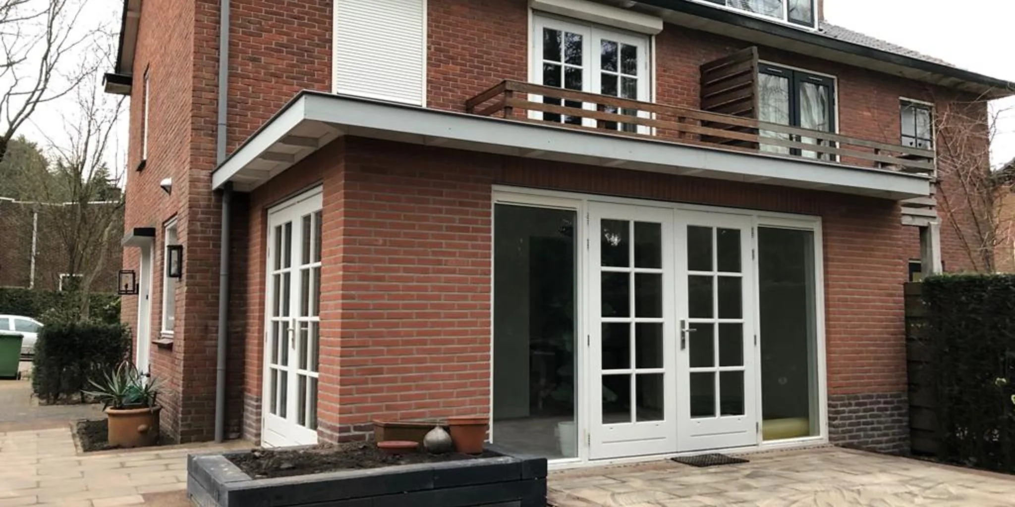 Afgeronde aanbouw met witte openslaande deuren en balkon aan bakstenen woning, opgeleverd door AanbouwMaximaal