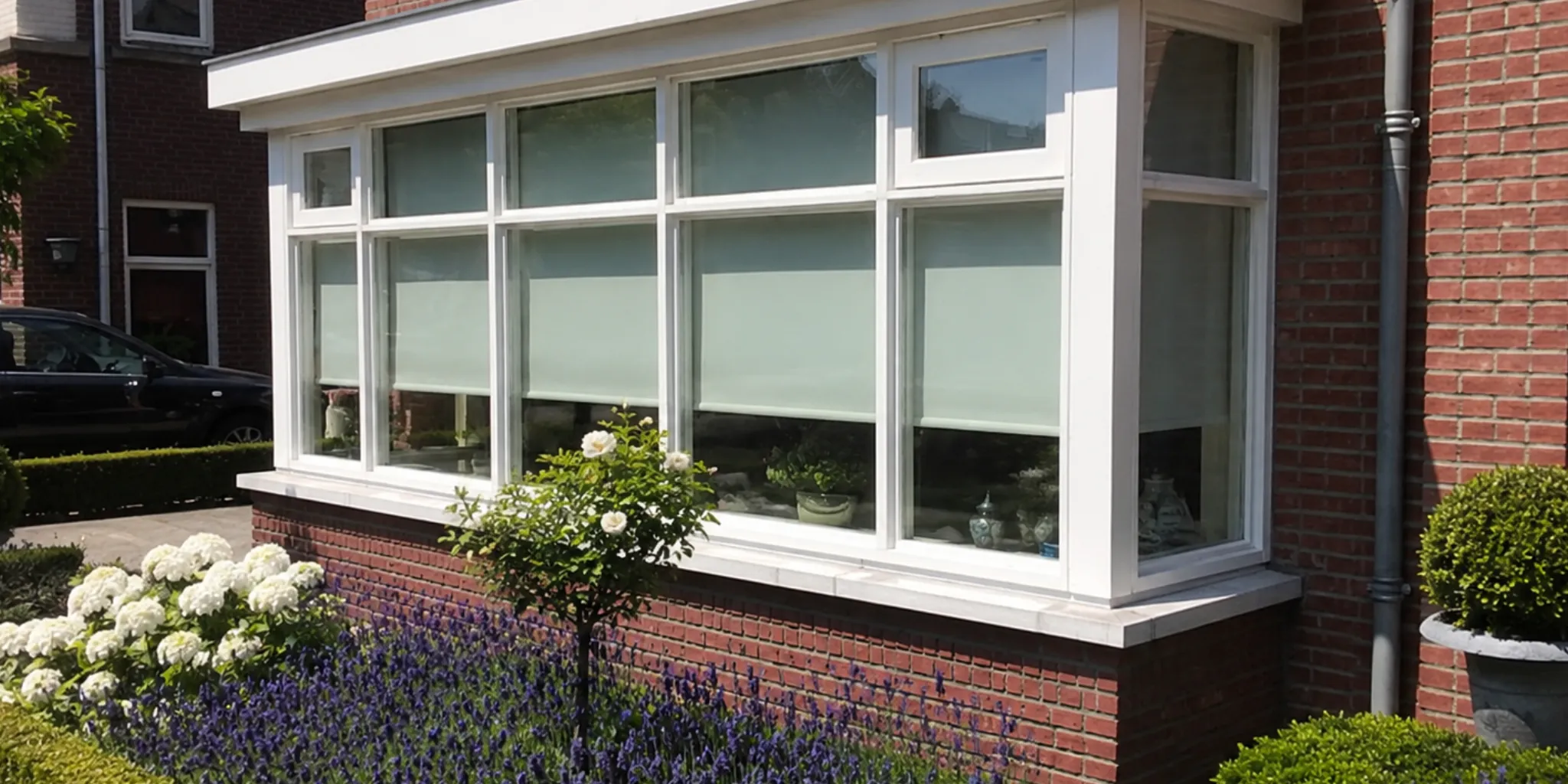 Witte erker met grote ramen aan de voorgevel van een woning met rode bakstenen, omringd door hortensia's en lavendel in de voortuin