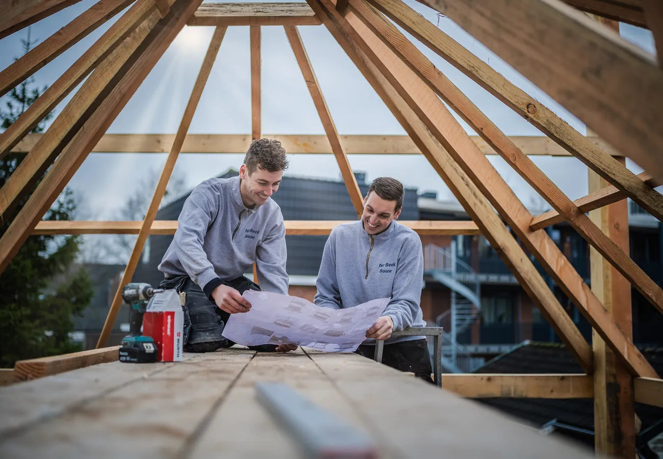 Twee bouwvakkers bekijken samen de bouwtekening op de dakconstructie van een aanbouw