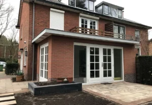 Bakstenen aanbouw aan de achterzijde van een woning, met openslaande tuindeuren die toegang geven tot het terras