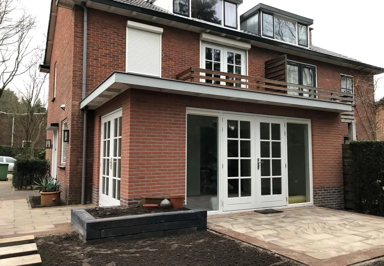 Bakstenen aanbouw aan de achterzijde van een woning, met openslaande tuindeuren die toegang geven tot het terras
