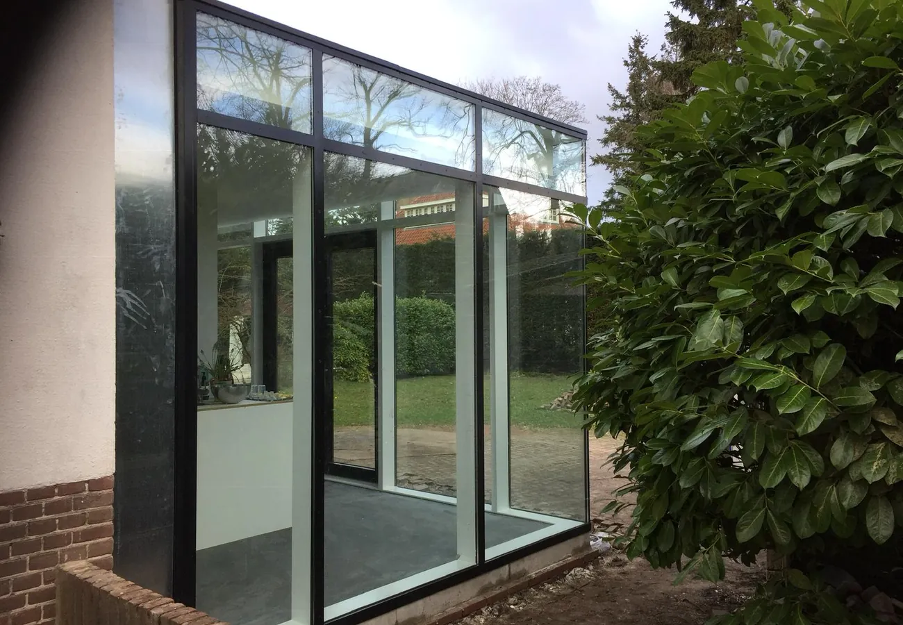 Moderne glazen aanbouw met grote raampartijen aan de achterzijde van een woning, met vrij uitzicht op de tuin