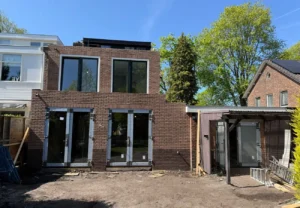 Afgebouwde aanbouw als thuiskantoor met bakstenen gevel, grote raampartijen en openslaande tuindeuren, gefotografeerd op een zonnige dag in de afrondende bouwfase.