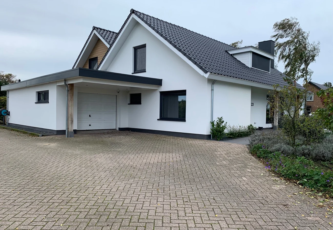 Afgeronde witte aanbouw met schuin dak aan een vrijstaande woning, gerealiseerd door AanbouwMaximaal